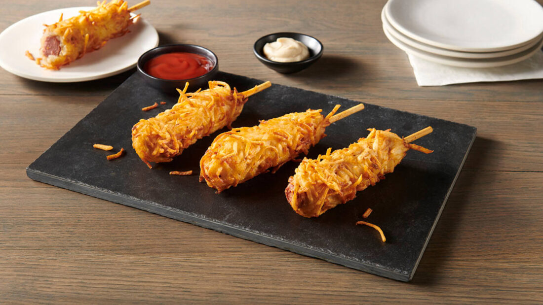 Crispy Korean potato cheese corndogs served on a black slate board with ketchup and creamy dipping sauce
