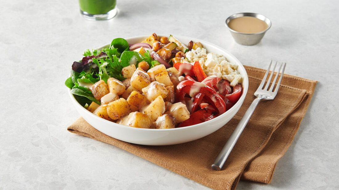 Mediterranean-style build-your-own potato power bowl with diced potatoes, greens, tomatoes, chickpeas, feta, sauce, and green smoothie