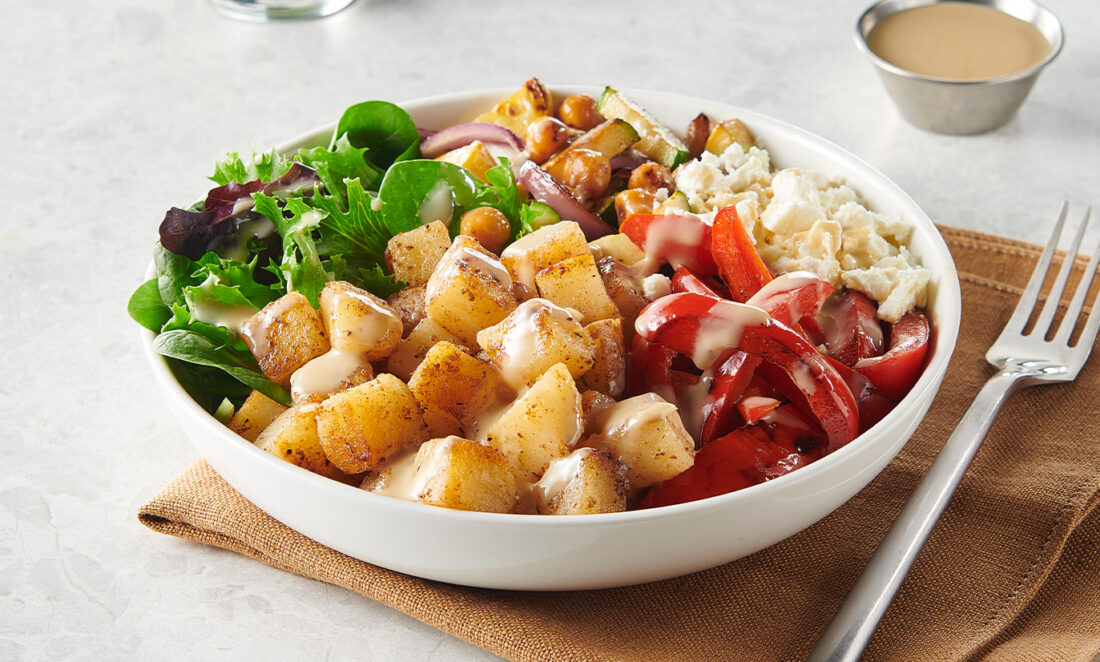 Mediterranean-style build-your-own potato power bowl with diced potatoes, greens, tomatoes, chickpeas, feta, sauce, and green smoothie