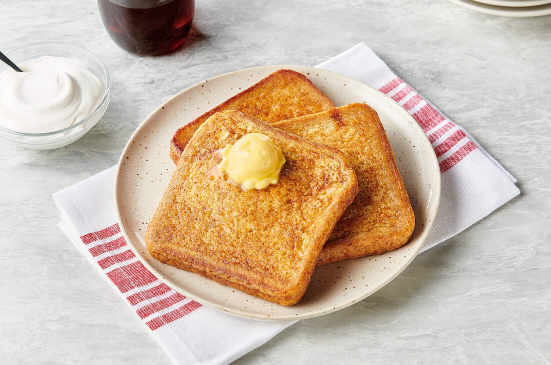 Golden French toast slices topped with butter on a plate with syrup and cream, highlighting French toast as an all-day menu option.